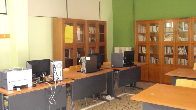 Μια ευρύχωρη αίθουσα βιβλιοθήκης με τοίχους σε ανοιχτό πράσινο χρώμα. Στο κέντρο υπάρχουν δύο μεγάλα ξύλινα τραπέζια με συνολικά οκτώ κίτρινες καρέκλες γύρω τους. Τα τραπέζια είναι άδεια εκτός από μερικά διάσπαρτα χαρτιά και ένα μαύρο σταθερό τηλέφωνο στο πλησιέστερο τραπέζι. Στα δεξιά, τρεις επιτραπέζιοι υπολογιστές βρίσκονται σε μικρότερα ατομικά γραφεία, καθένα με μια μαύρη καρέκλα γραφείου. Ο πίσω τοίχος είναι επενδυμένος με μια μεγάλη ξύλινη βιβλιοθήκη γεμάτη με βιβλία διαφόρων μεγεθών και χρωμάτων. Η αίθουσα φωτίζεται καλά από φυσικό φως που προέρχεται από εκτός κάμερας, πιθανώς από παράθυρα που δεν είναι ορατά σε αυτή την άποψη.